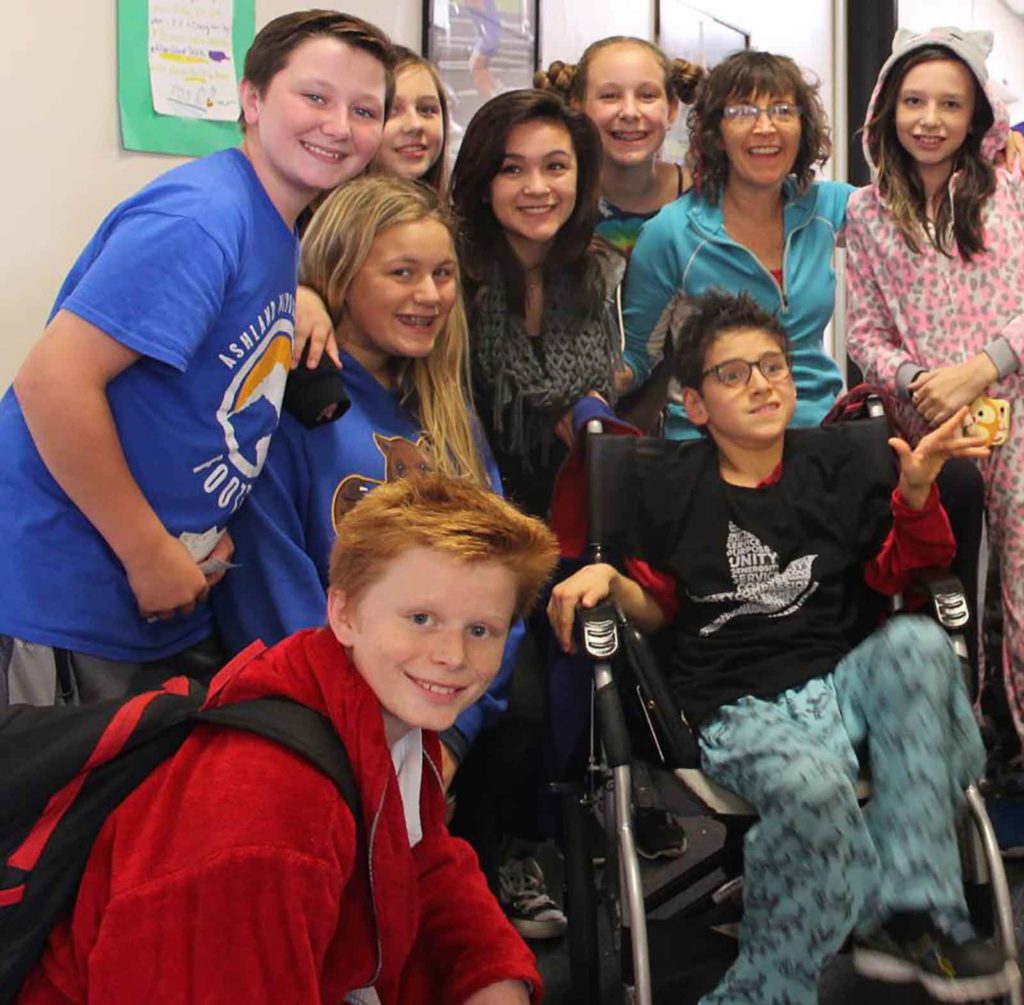 Sparrow, Luke, sits in a wheel chair smiling and surrounded by friends.
